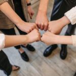 A close-up of five people fist bumping, symbolizing teamwork and unity indoors.